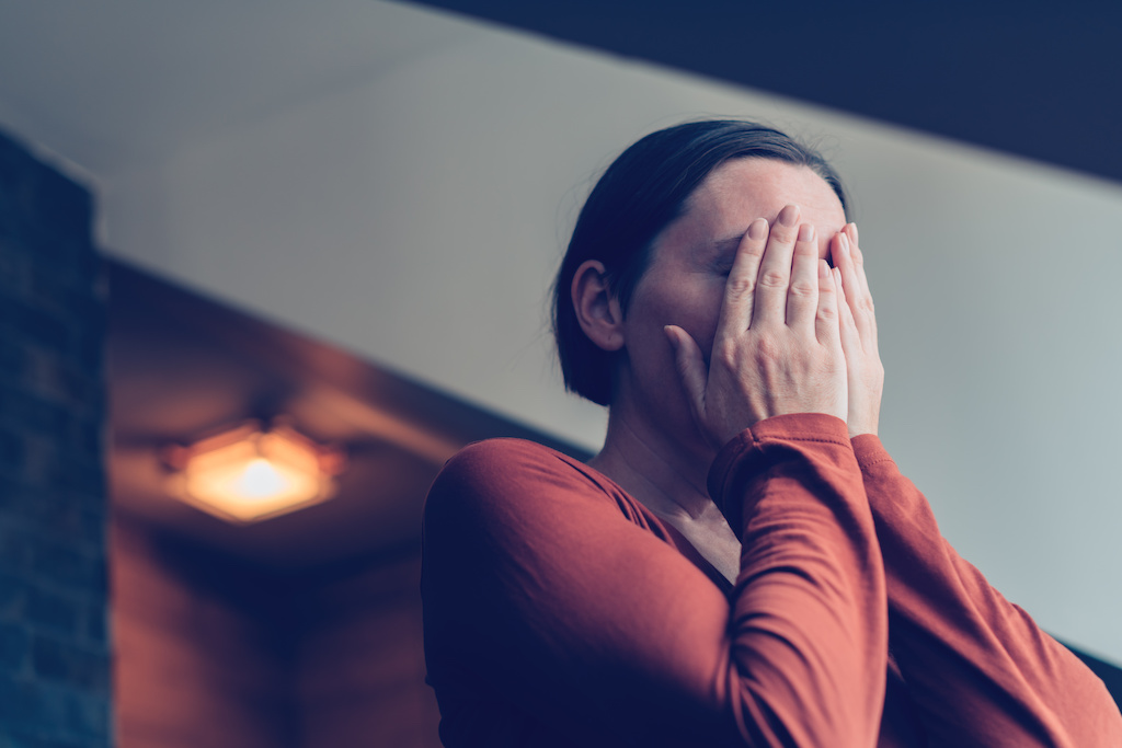 Depressed woman covering face with hands and crying in loft apartment, selective focus